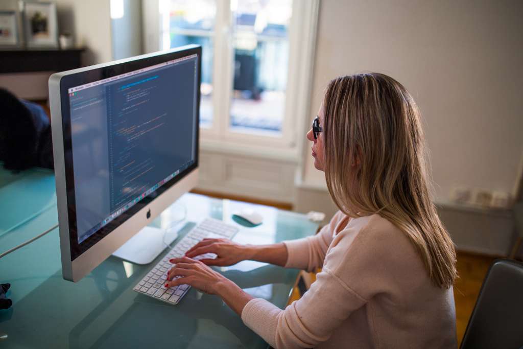 woman sitting at a desk working on code on a large desktop computer