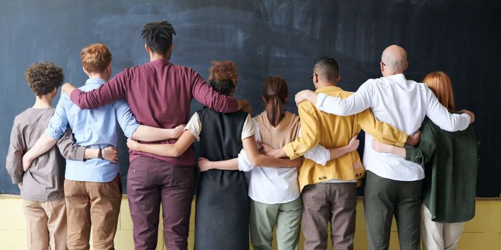 diverse group of adults standing facing away from the camera with arms around each other's backs